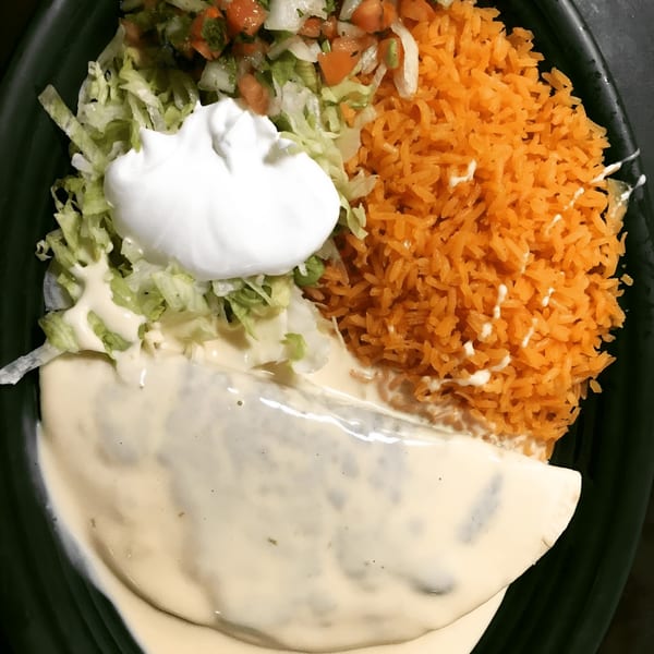 A Mexican dish with a quesadilla covered in white sauce, orange rice, lettuce, pico de gallo, and sour cream.