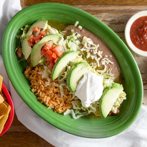 Los Compas Raytown's enchiladas with rice, beans, avocado, sour cream, and salsa on a green plate.