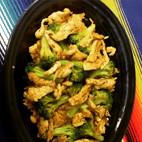 Chicken and broccoli stir-fry in a black bowl, on a colorful striped tablecloth.