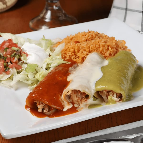 Two enchiladas, one red and one green, with rice, lettuce, pico de gallo, and sour cream.