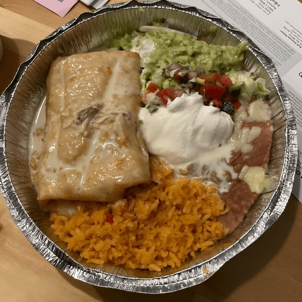 A Los Compas Raytown Mexican burrito with rice, beans, guacamole, and sour cream in a foil container.