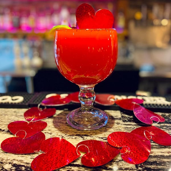 A vibrant red margarita in a goblet, garnished with a lime and a heart, surrounded by heart-shaped confetti.